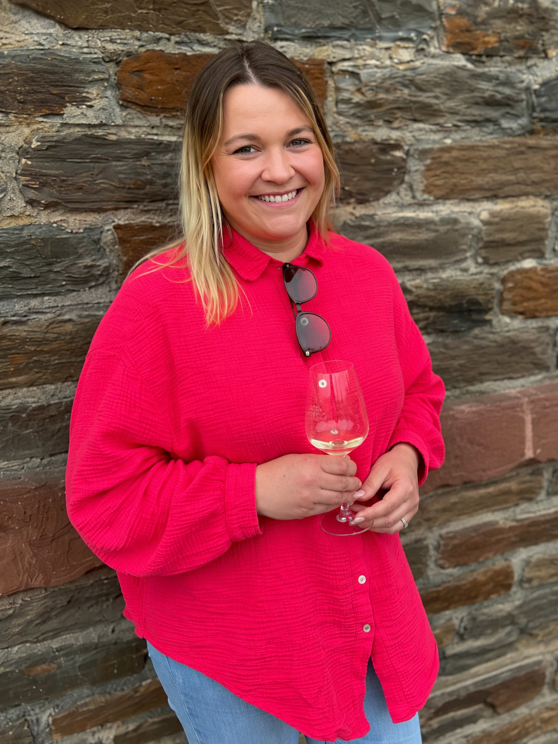 Porträt von Luca in pinker Bluse mit Weinglas vor einer typischen Schiefersteinwand – persönlich, modern und nahbar für MOS:L wein:events.