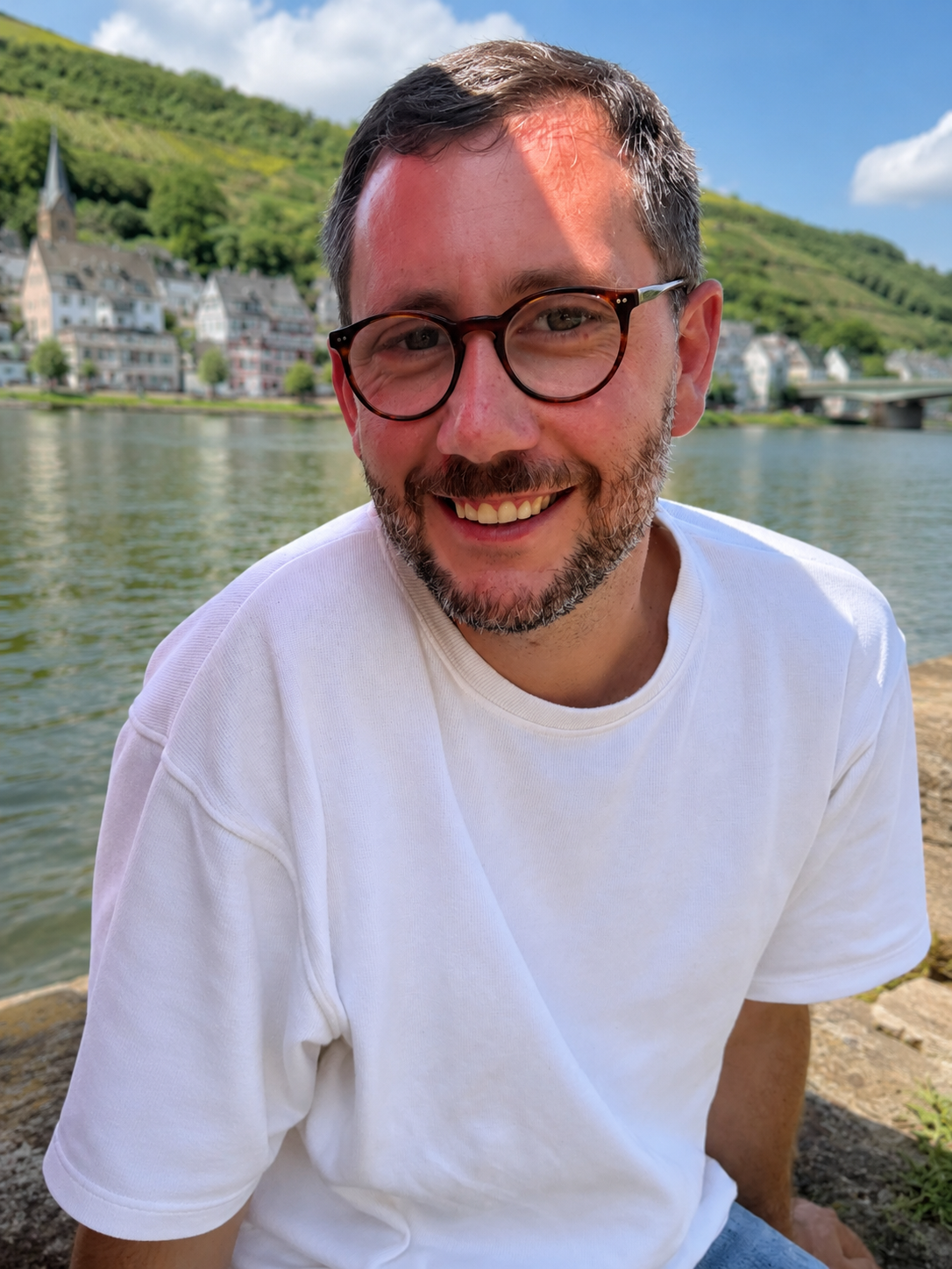 Porträt von Simon am Ufer der Mosel mit Blick auf Fluss, Weinberge und einen Moselort – authentisch und persönlich für MOS:L wein:events.
