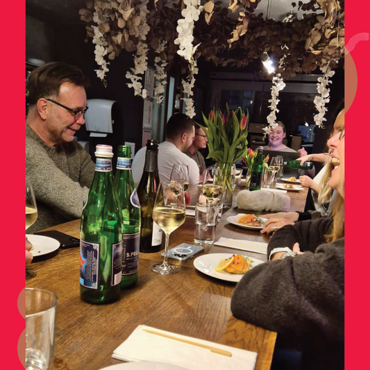 Gäste sitzen gemeinsam an einer langen Tafel mit Wein, Wasser und kleinen Speisen bei einer Rebenreise Mosel Weinprobe in der Weinlounge Zell.